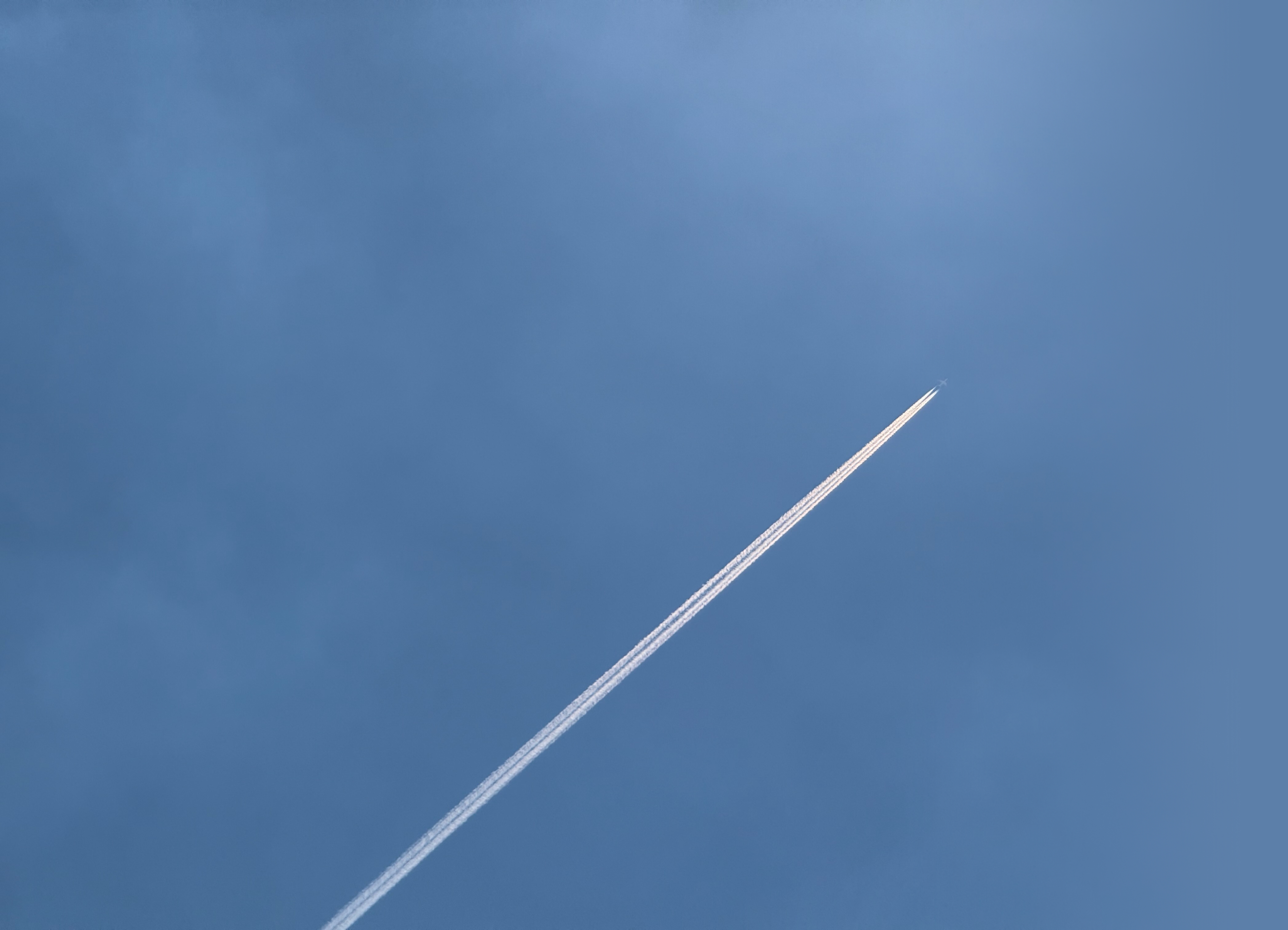 A plane trail rising across a blue sky.